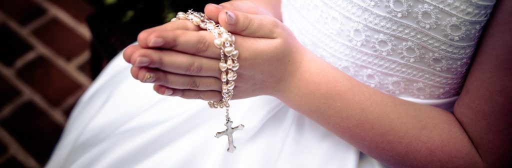 Girl's hands folded in prayer and holding rosary.